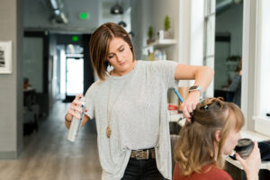 a hair stylist in a salon with a customer sitting in the styling chair