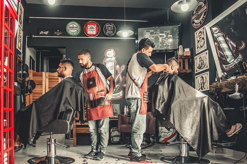 two barbers giving their customers hair cuts and beard trims in a salon